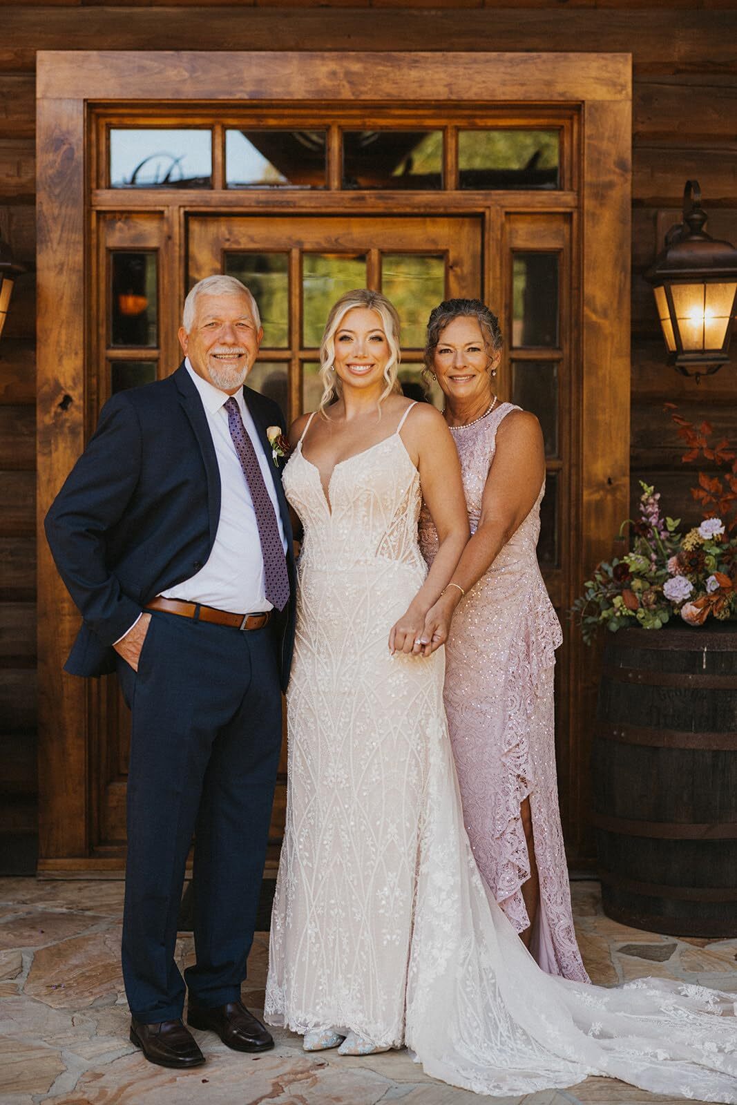 Mother of the bride wearing a blush tea length dress with daughter at a rustic outdoor wedding