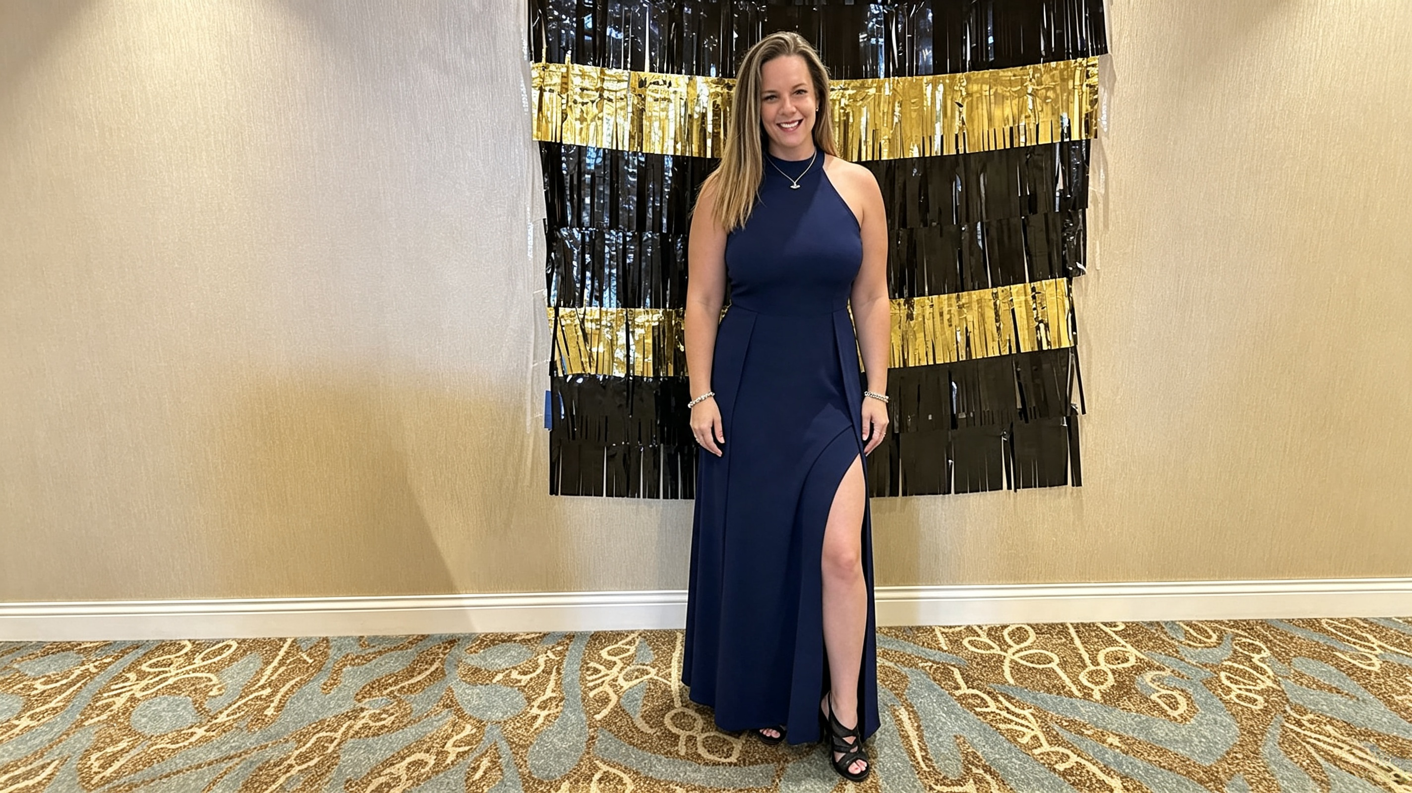Woman wearing a navy halter gown with high slit in front of a formal event backdrop